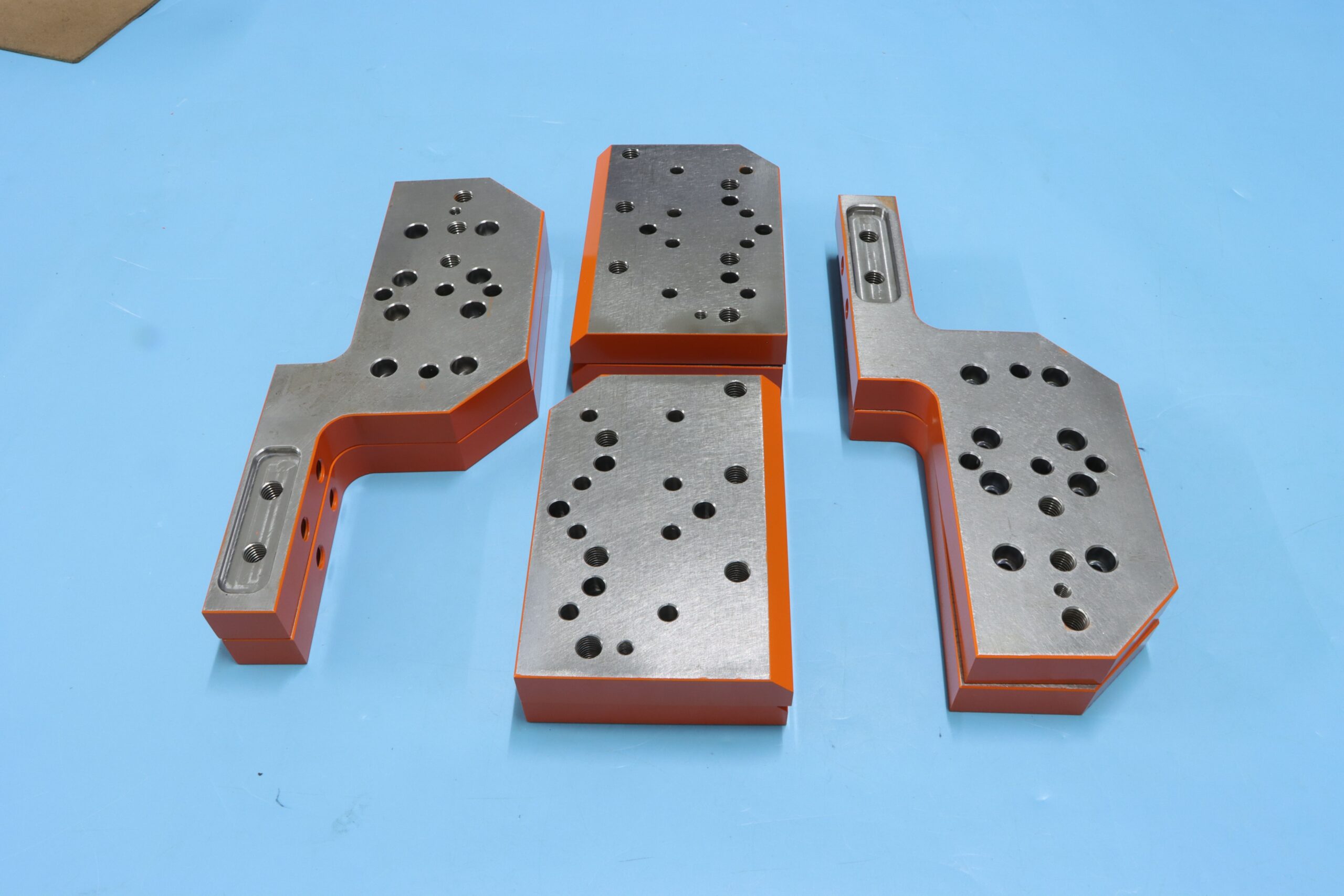Precision custom machined die tool steel blocks with vibrant orange painted edges and multi-hole alignment.