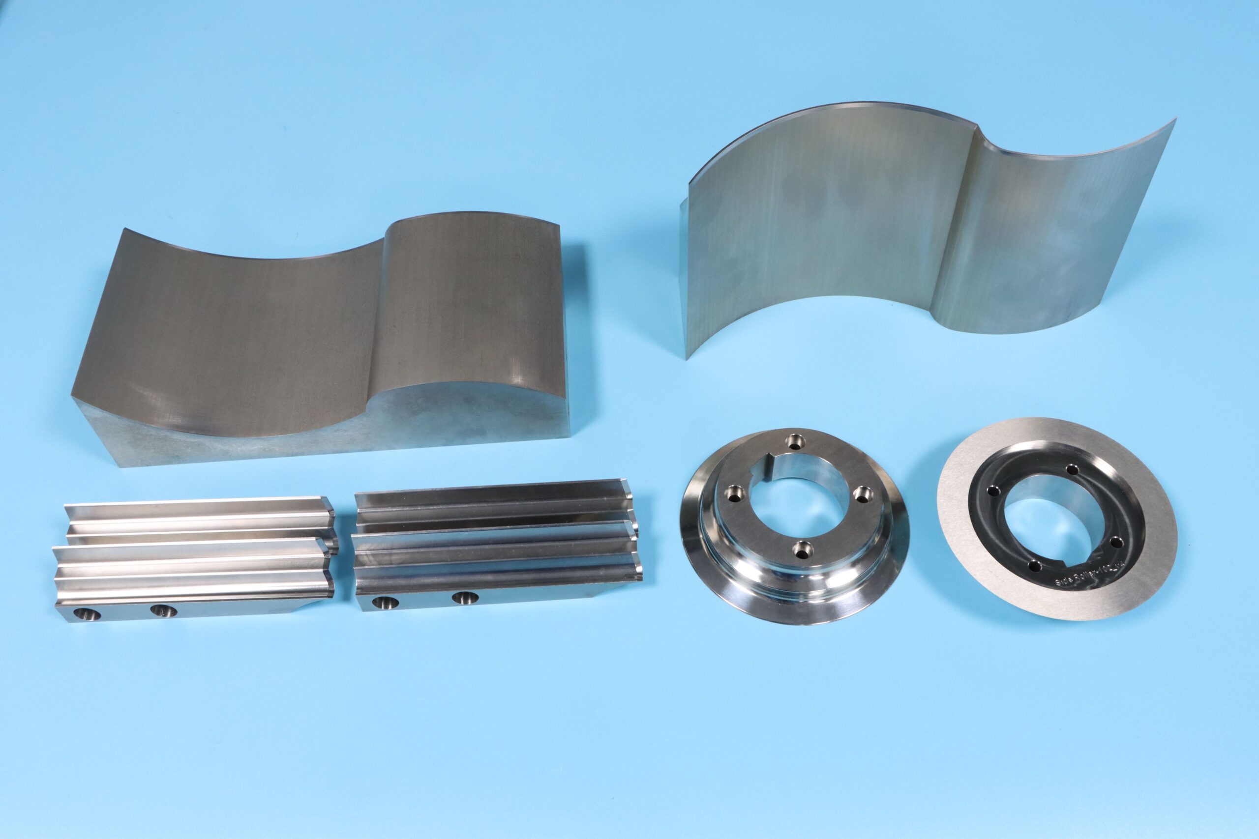 Custom heat-treated steel machinery components including curved guide plates and turned collars.